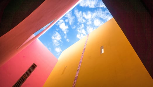 Blue sky with clouds visible through a space between colorful buildings