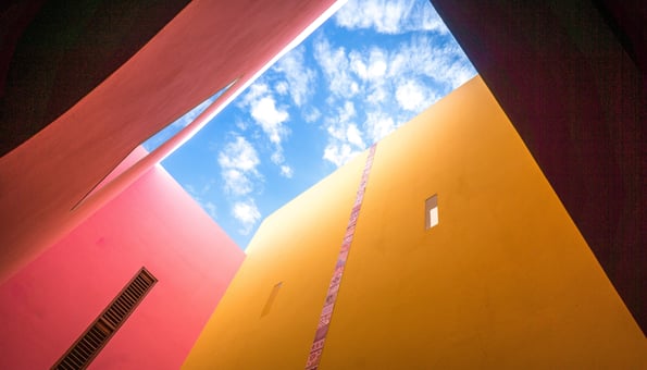 Blue sky with clouds visible through a space between colorful buildings