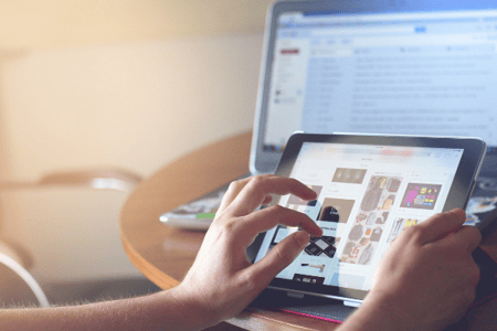 personne sur sa tablette avec un ordinateur ouvert en arrière plan
