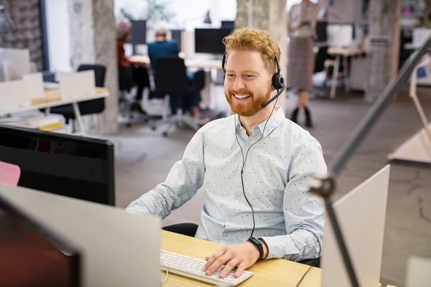 Kundendienstmitarbeiter sitzt mit Headset vor Computer und lächelt
