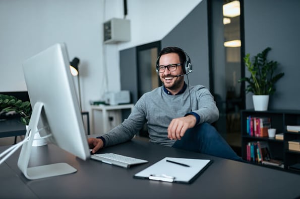 Mann mit Headset sitzt am Schreibtisch und lacht