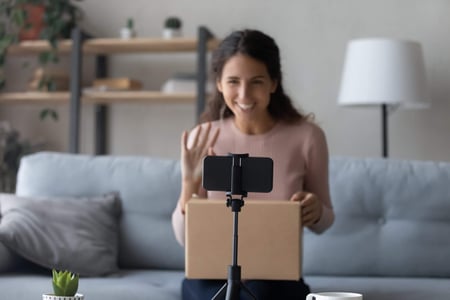 Frau öffnet Paket und filmt sich mit dem Smartphone