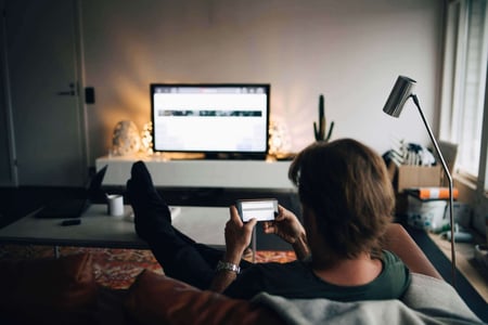 Mann-sitzt-mit-Smartphone-auf-der-Couch-und-schaut-Fernsehen