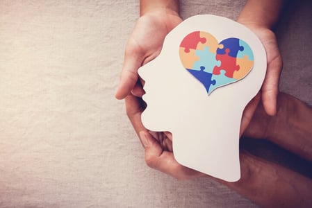 Menschliche Haende halten einen Kopf aus Pappe mit einem Herz als Gehirn als Symbol fuer Neuromarketing