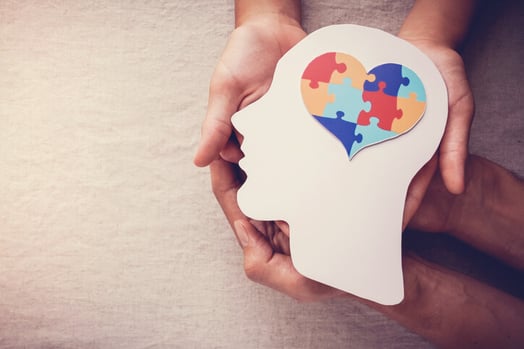 Menschliche Haende halten einen Kopf aus Pappe mit einem Herz als Gehirn als Symbol fuer Neuromarketing