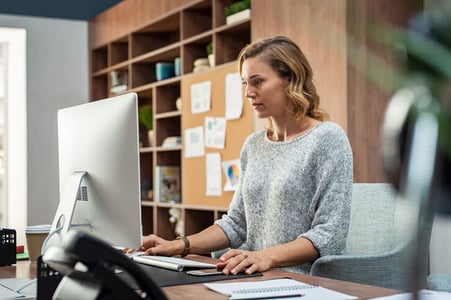 Frau sitzt am Schreibtisch und arbeitet an einem Computer