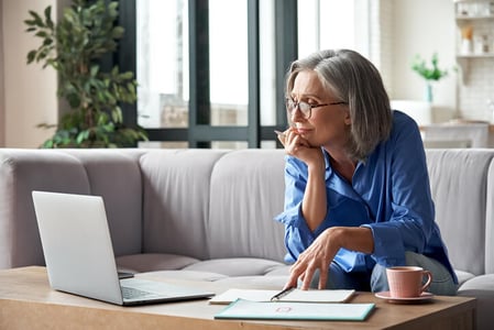 Frau mit Brille sitzt auf Sofa und schaut auf ihren Laptop