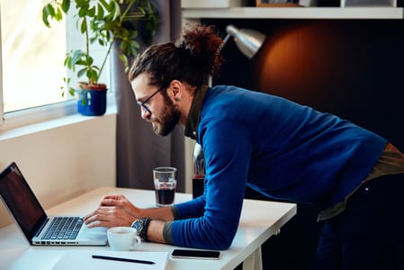 Mann steht am Schreibtisch und arbeitet an seinem Redaktionsplan am Laptop
