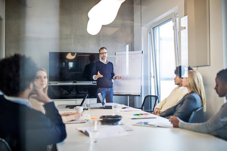 Mitarbeiter spricht ueber Dienstleistungsmarketing vor Team in Meeting-Raum