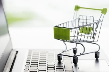 Grüner Einkaufswagen auf einem Laptop als Symbol für Green Marketing