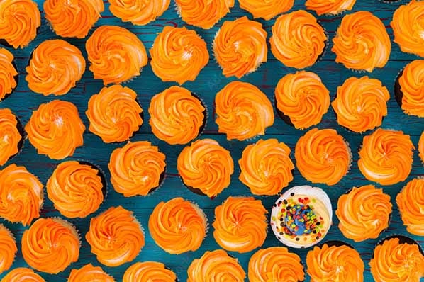 Mehrere orangefarbige Cupcakes und ein bunter Cupcake
