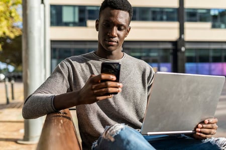 Mann draussen mit Laptop liest Newsjacking Nachrichten auf Smartphone