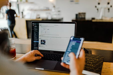 Person nutzt praktische Slack-Apps am Handy und Laptop