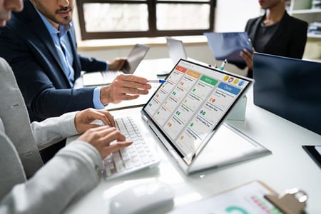 Mitarbeitende am Tisch vor Tablet nutzen Projektmanagement-Tools