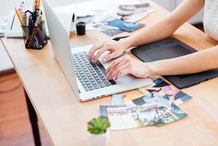 Closeup of hands of young woman photograper typing on laptop keyboard and using graphic tablet