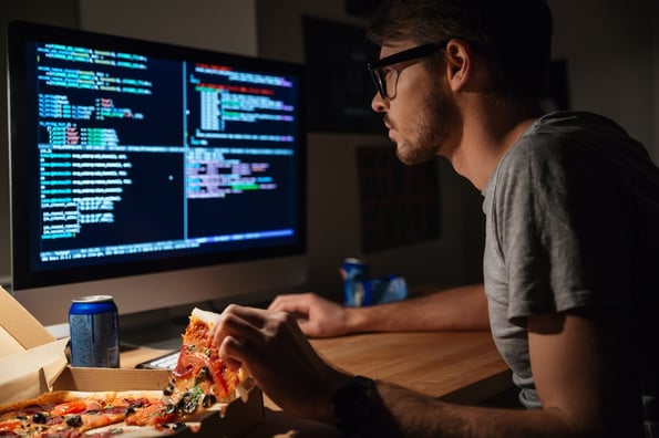 Profile of concentrated young software developer eating pizza and coding at home.jpeg