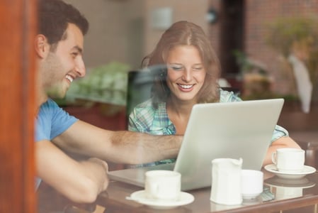 Two laughing students looking at laptop in college canteen.jpeg