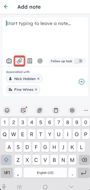A screenshot on Android. A note pop-up  box is displayed. A paperclip icon for attachments is highlighted in orange. The note is associated with "Nick Halden" and "Fine Wines." A virtual keyboard occupies the lower part of the screen.