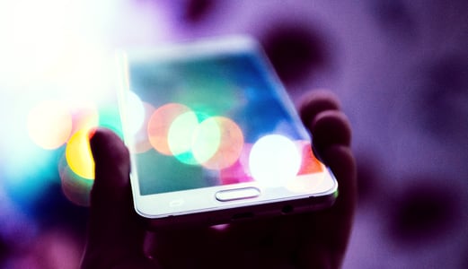 White phone held in hand with purple swirls in the background and multi-colored light reflecting off of phone's screen