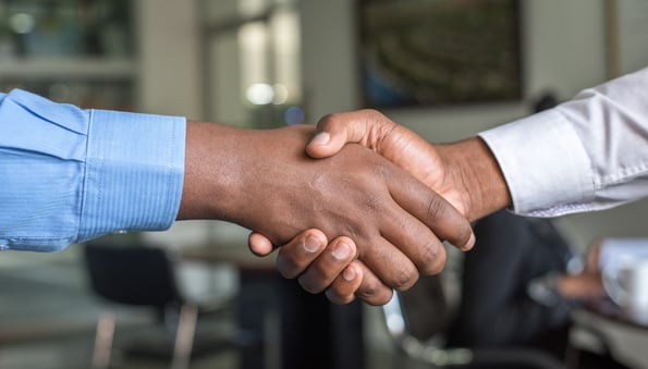 Two hands with cuffed blue sleeves grasped in a handshake.