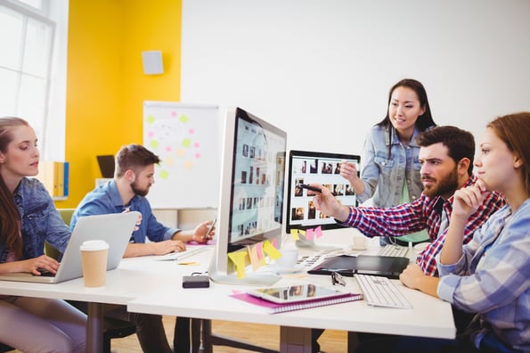 A team collaborating on one computer while another teammate works on a different computer in the background