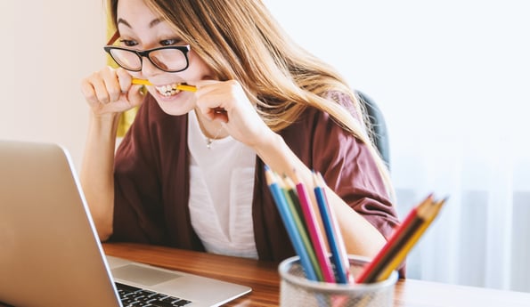Stressed woman biting pencil while staring at computer screen trying to bid manually