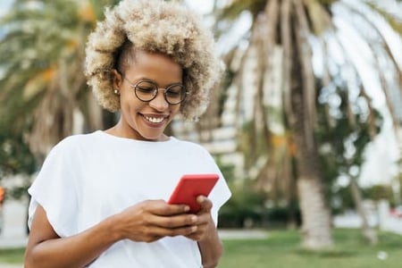 A woman stands outside while browsing Twitter alternatives on her phone. 