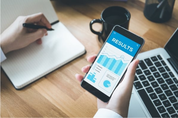 bureau gros plan sur des mains tenant un smartphone qui affiche les graphiques mesurant des résultats