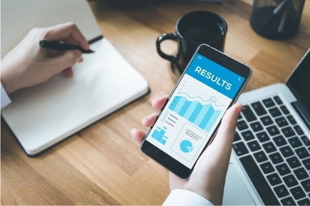 bureau gros plan sur des mains tenant un smartphone qui affiche les graphiques mesurant des résultats