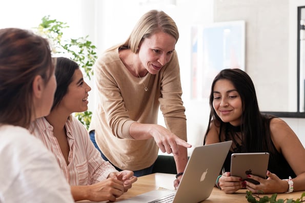 Four women of varying ethnicities discussing content on Mac computer screen