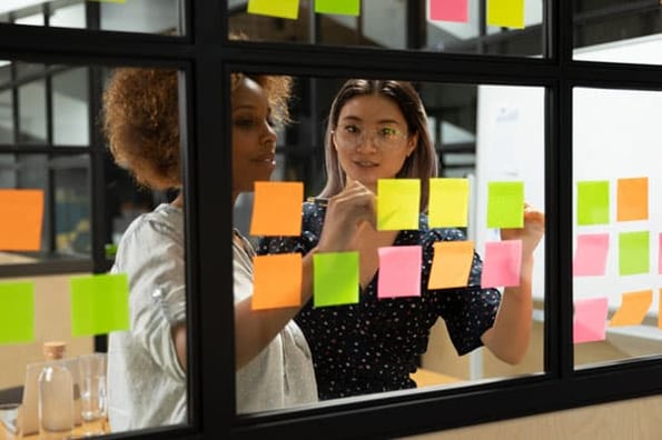 Two women use sticky notes to boost productivity at work.