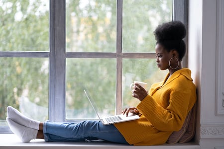 woman sitting in a windowsill using a laptop to use a tool for finding long-tail keywords