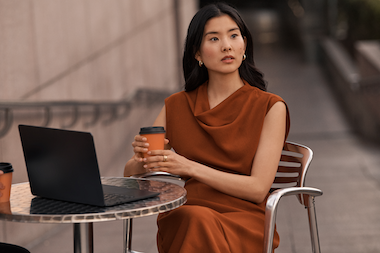 Frau sitzt vor Laptop mit Kaffee in der Hand