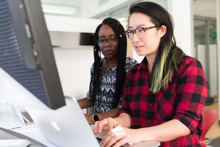 Two people reviewing workflows on monitor and laptop screens