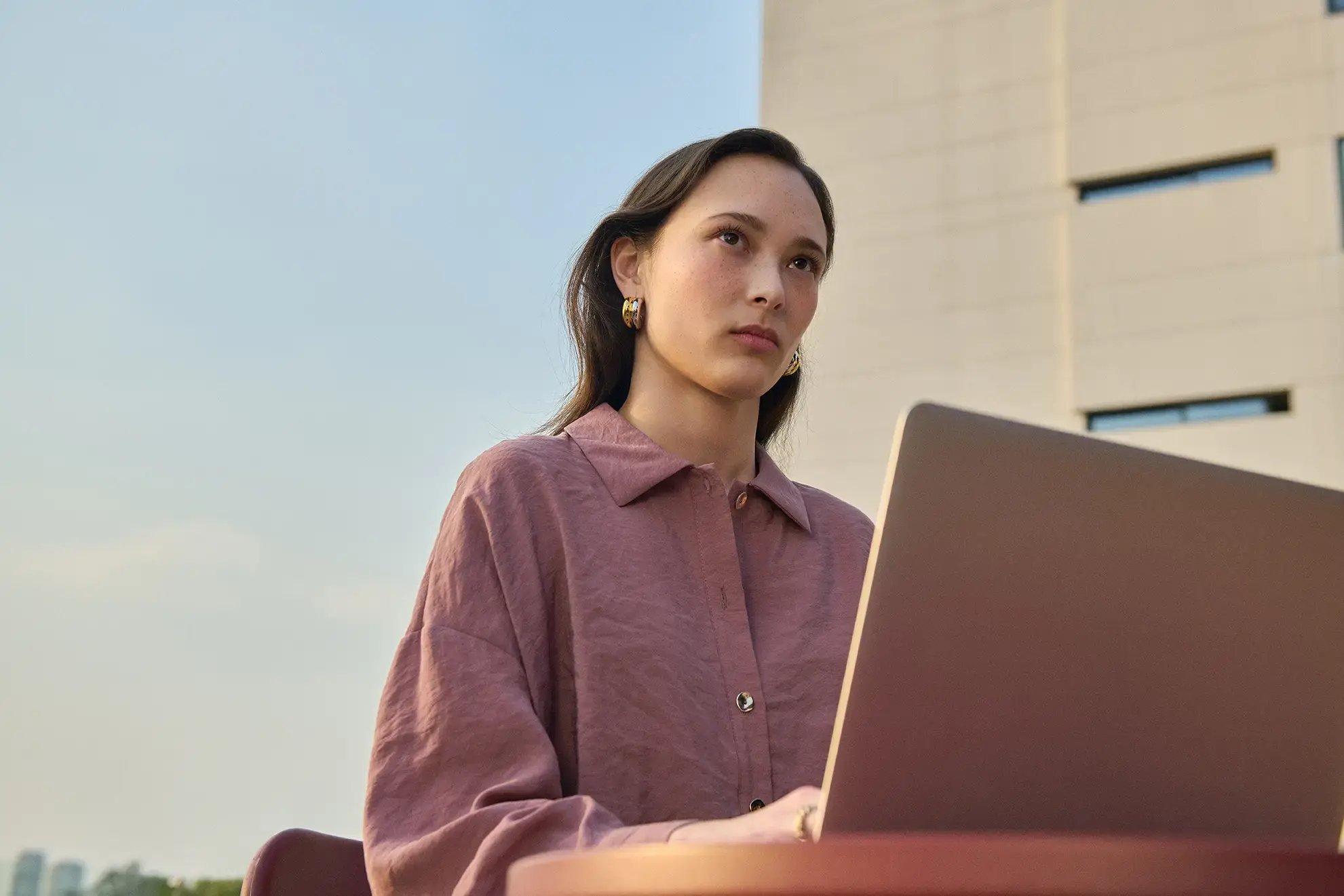 Junge Frau arbeitet konzentriert an einem Laptop im Freien vor einem modernen Gebäude