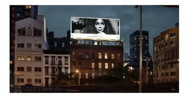 how to create a marketing strategy, A nighttime city street with a large billboard displaying a womans portrait, an example of paid media.
