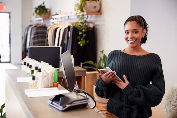 Happy business owner running a successful clothing retail business using her mobile phone and computer.