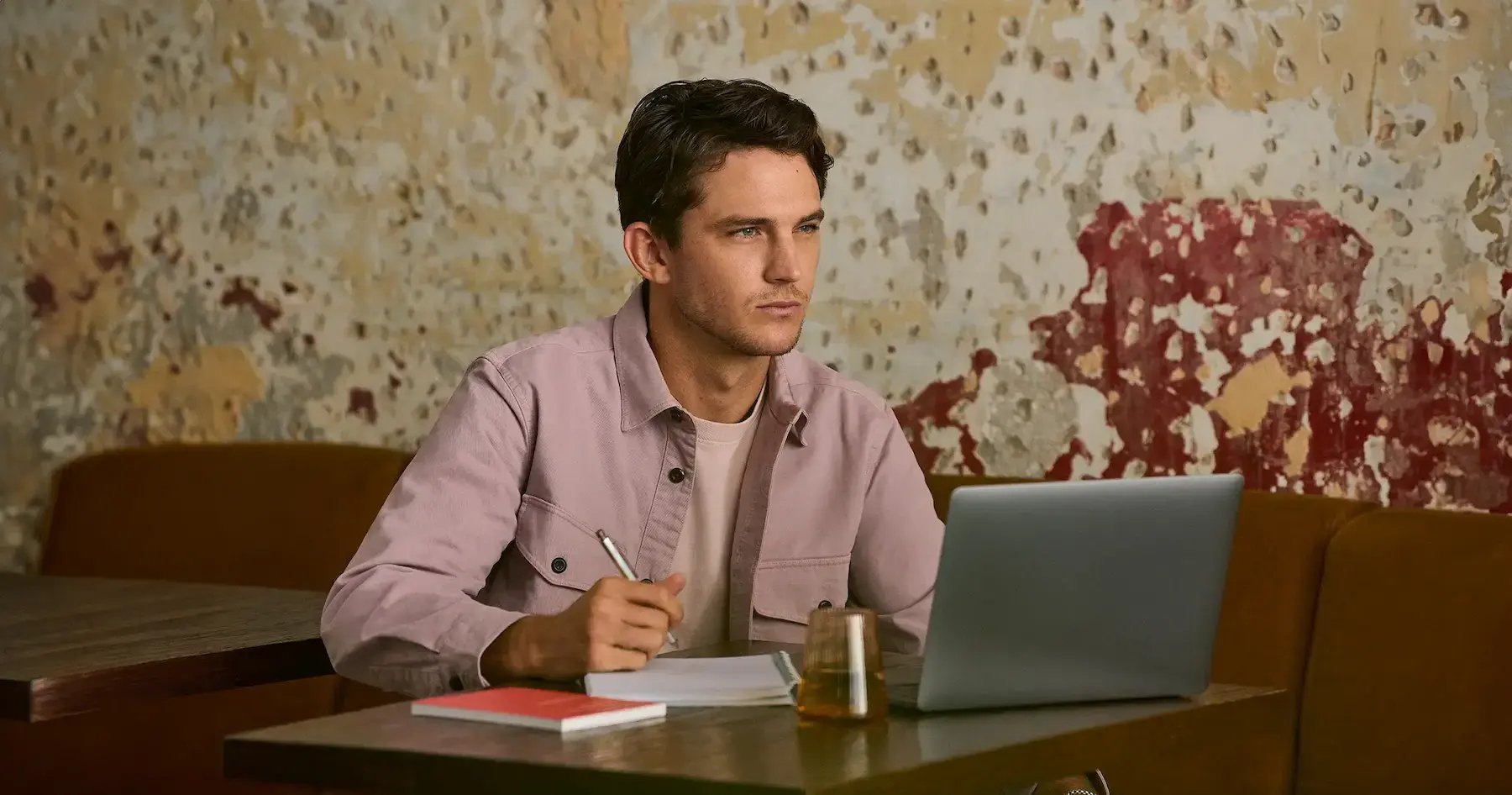 Mann arbeitet konzentriert an einem Laptop und macht sich Notizen in einem modernen Café