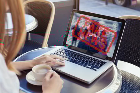 mulher navega internet em seu laptop, em um café. Monitor mostra aviso sobre Fake News