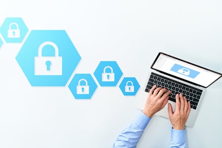 imagem mostra mãos masculinas digitando em um laptop - cadeados representando informações criptografadas aparecem tanto na tela do laptop como na mesa em que o computador está 