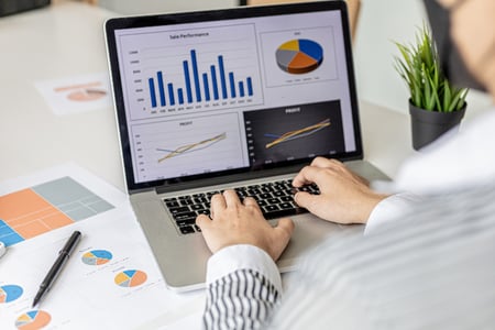 Imagem mostra homem digitando informações em um laptop. Tela mostra gráficos em diferentes tamanhos e formatos. 