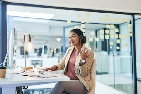 Vendedora utilizando a metodologia de vendas inbound para atender cliente. Ela está em um escritório, sentada em frente ao computador e falando ao telefone