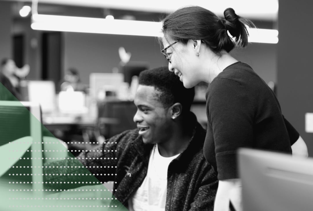 Schwarzweißbild zweier Personen, die sich unterhalten und dabei auf einen Computerbildschirm schauen