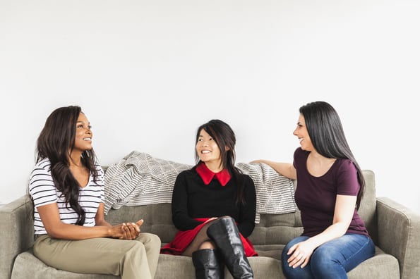 three-models-share-a-smile-on-a-grey-sofa