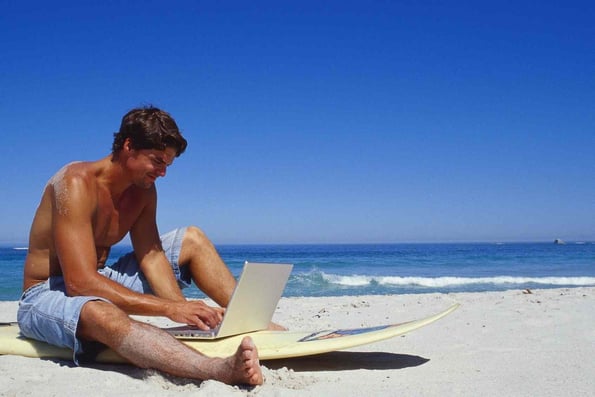 homem acessa informações do trabalho em laptop na praia - como se manter atualizado no trabalho em viagens
