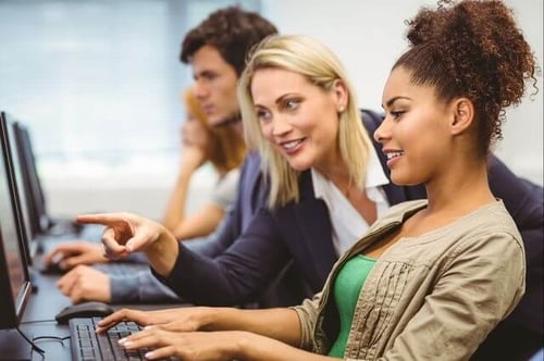 Professora de marketing apontando para a tela do computador de uma aluna durante uma aula sobre texto alternativo