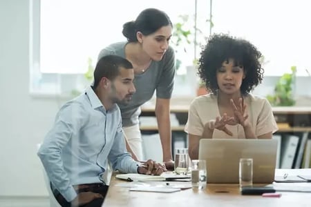 group of coworkers sitting around a laptop computer talking about wordpress plugins to increase traffic
