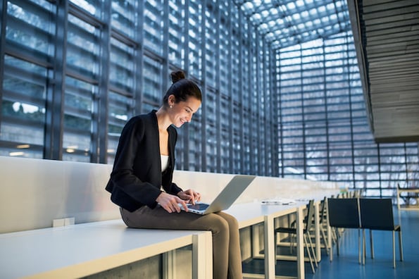 woman sitting in an office using a laptop to install a wordpress tech blog theme