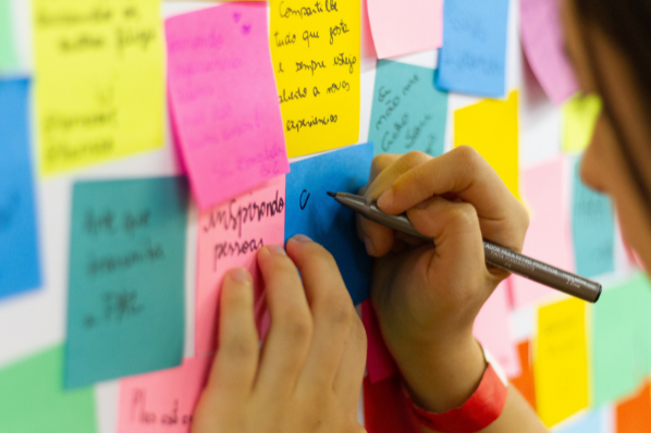Mains entrain d'écrire sur un post-it accroché à un mur 
