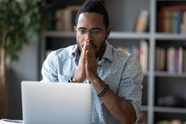 Marketer with a shocked expression at his laptop because he accidentally posted the wrong thing on Facebook